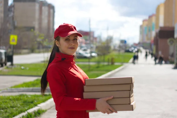 Pizza delivery. The food delivery girl is holding five boxes of pizza. She holds the boxes forward and smiles.