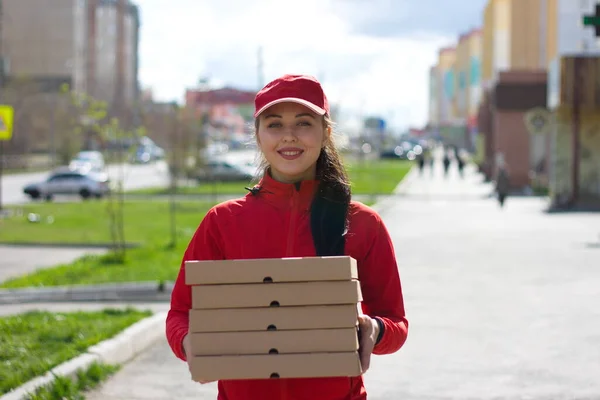 Pizza delivery. The food delivery girl is holding five boxes of pizza. She holds the boxes forward and smiles.