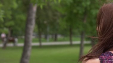 Parktaki bir kızın portresi. Ağır çekim 2x. Güzel bir kızın profilindeki yüz. Sırtı dönük durur, sonra başını çevirir ve başka yere bakar..