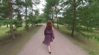 Parktaki kız. İnce, uzun boylu bir kız, kozalaklı ağaçların arasında parkta yürüyor..