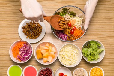 Böcekler ile-taze sebze salatası sebze salatası ile solucan böcekler ahşap bir masa üzerinde mutfakta yemek insan kadın eller. Sağlıklı yemek yüksek protein diyet kavramı. Üstten görünüm. Seçici odak.