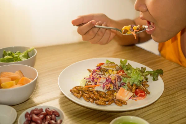 The boy is eating insects food - The boy is eating vegetable salad with worm insects on wooden table delicious and happy. Healthy meal high protein diet concept.