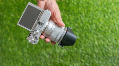 El bir kamera yeşil çim zemin üzerine tutarak fotoğrafçı el bir fotoğraf makinesi - kapat dayanabiliyor. Yakın çekim, seçici odak.