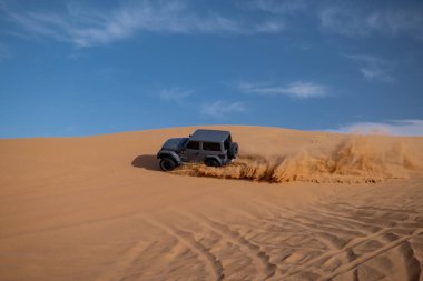 Suudi Arabistan 'da kum tepelerinde Jeep off-road sürüyor. Suudi Arabistan 'daki altın çöl kum tepelerinden geçen siyah Jeep SUV. Off-road macera, çöl keşfi ve açık mavi gökyüzünün altında 4x4 güç. Yüksek