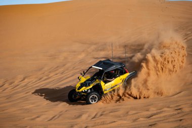 Suudi Arabistan 'da çölde bir arazi aracı. Sarı arazi aracı Suudi Arabistan çölünde kum tepecikleri boyunca sürüp bir toz bulutu yaratıyor. Ekstrem macera ve çöl motorsporu