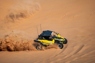 Suudi Arabistan 'da çölde bir arazi aracı. Sarı arazi aracı Suudi Arabistan çölünde kum tepecikleri boyunca sürüp bir toz bulutu yaratıyor. Ekstrem macera ve çöl motorsporu