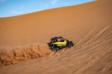 Suudi Arabistan 'da çölde bir arazi aracı. Sarı arazi aracı Suudi Arabistan çölünde kum tepecikleri boyunca sürüp bir toz bulutu yaratıyor. Ekstrem macera ve çöl motorsporu