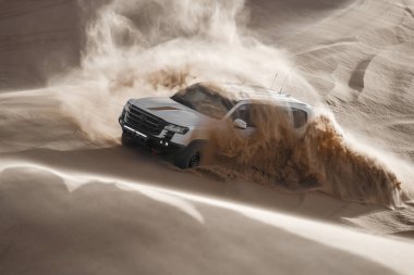 Suudi Arabistan 'da çölden geçen beyaz bir SUV. Güçlü beyaz SUV Suudi Arabistan 'daki çöl kumullarında hızla ilerliyor. Off-road macera, 4x4 araç, ve açık hava keşfi Arabistan 'da