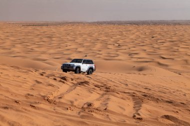 Suudi Arabistan 'da çölden geçen beyaz bir SUV. Güçlü beyaz SUV Suudi Arabistan 'daki çöl kumullarında hızla ilerliyor. Off-road macera, 4x4 araç, ve açık hava keşfi Arabistan 'da