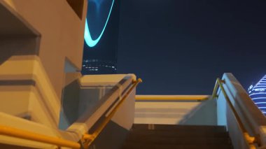 Riyad, Suudi Arabistan 'daki Krallık Merkez Kulesi. Riyad, Suudi Arabistan 'daki palmiye ağaçları tarafından çerçevelenmiş ikonik Krallık Merkezi Kulesi' nin gece görüşü. Aydınlatılmış gökdelen en büyük şehirlerden biridir.