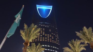 Riyad, Suudi Arabistan 'daki Krallık Merkez Kulesi. Riyad, Suudi Arabistan 'daki palmiye ağaçları tarafından çerçevelenmiş ikonik Krallık Merkezi Kulesi' nin gece görüşü. Aydınlatılmış gökdelen en büyük şehirlerden biridir.