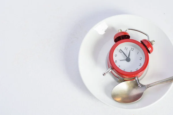 Reloj despertador rojo en placa blanca con una cuchara de plata — Foto de Stock