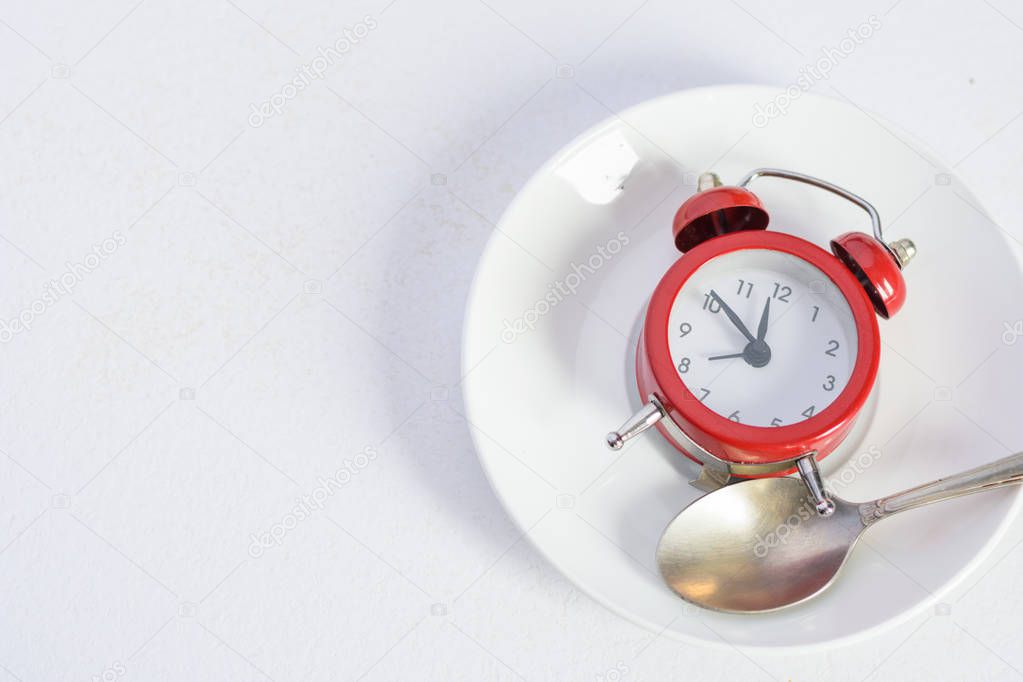 Red alarm clock on white plate with a silver spoon