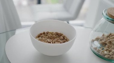 A close-up of a white bowl filled with granola on a table, promoting healthy breakfast and nutrition. Healthy Breakfast Bowl with Granola on a White Table