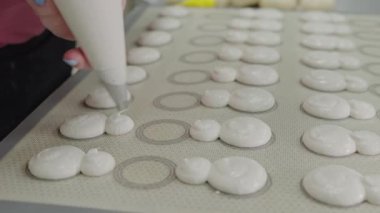 Close-up view of a pastry chef skillfully piping batter for macarons onto a baking sheet in a commercial kitchen, focusing on precision and quality. Pastry Chef Preparing Handmade Macarons