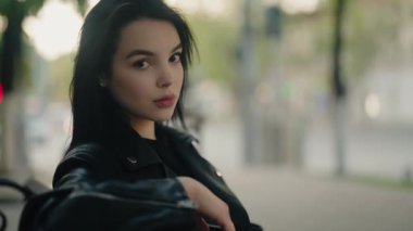 Portrait of a confident young woman in a black leather jacket outdoors in an urban setting with a blurred background. Confident Young Woman in Leather Jacket Outdoors in Urban Setting