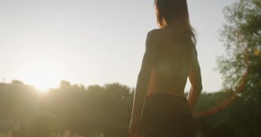Back view on sporty woman has workout outdoors and training with resistance band in hands. Athletic woman goes in for sports with resistance band. Woman pumping her biceps muscles.