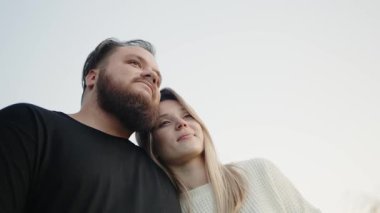 A young couple in a tender embrace, looking into the distance. The image captures a sense of love and companionship in a serene outdoor setting. Young Couple Enjoying a Romantic Moment Together
