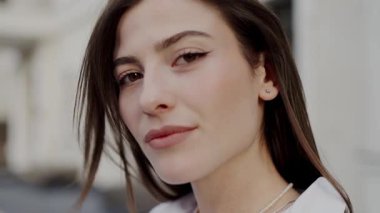 A close-up image showing a young woman with brown hair giving a salute. She appears calm and composed, with a soft focus background hinting at an urban setting. Portrait of a Young Woman.