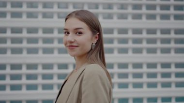 Portrait of a confident young woman with a subtle smile, dressed in a chic beige jacket, standing in front of a textured white wall. Confident Young Woman in Stylish Outfit by Modern Wall