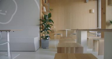 An inviting office cafeteria featuring contemporary wooden furniture and lush green plants promoting a clean and modern aesthetic. The space is perfect for breaks and informal meetings