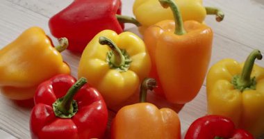 A close-up shot of various bell peppers in red, yellow, and orange on a light wooden surface. The peppers are fresh and vibrant, perfect for healthy cooking. Vibrant Fresh Vegetables
