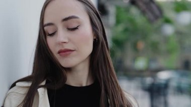 Close-up portrait of a young woman with long hair, looking confidently into the camera in an outdoor urban setting. Portrait Of Young Woman With Long Hair In Outdoor Urban Setting
