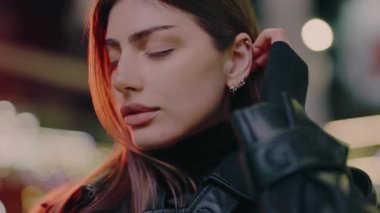 Portrait of a young woman against the background of night lights. Portrait luxury woman dusk street looking camera. Portrait of charming female. Model posing urban avenue. Beauty lady on street.