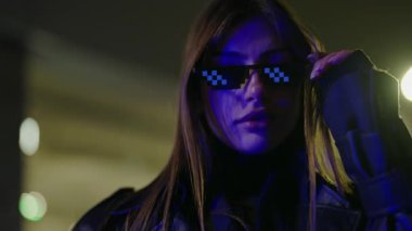 Confident attractive woman in leather coat and trendy glasses standing on stairs outdoors. Stylish female posing at night street. Young luxurious sexy woman looking at the camera outdoors.