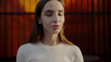 A thoughtful young woman poses in front of a striking orange industrial backdrop, showcasing a serene expression. Portrait of a Young Woman against an Orange Industrial Backdrop