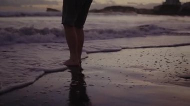 Close-up image of legs standing in ocean waves during a beautiful sunset at a Portugal beach. The scene captures serenity and the natural beauty of the seaside. Ocean Waves at Sunset