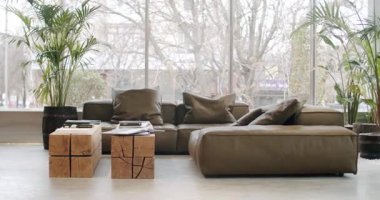 Modern living room interior with comfortable leather sofa and wooden coffee table. Large windows offer natural light, creating a cozy atmosphere. Plants and home decor complete the scene of a peaceful
