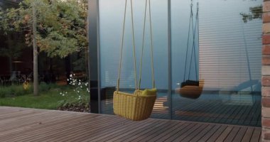A serene image showcasing a modern house exterior featuring a hanging basket chair on a porch with reflective windows overlooking a neatly landscaped yard.