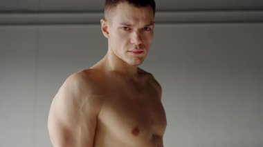 A powerfully built male athlete stands confidently in a gym, showing his well-defined muscles. His intense gaze adds to the motivation and dedication theme.