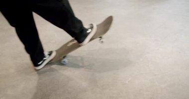 Close up shot of a person stopping and picking up their skateboard inside. Slow motion shot of a skateboarder wearing black pants and black picking up a skateboard with blue wheels and walking away.