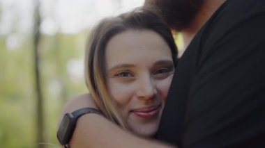A tender moment captured as a loving couple hugs in a sunny park. The image exudes warmth, comfort, and affection between two people. Loving Couple Embraces Under Sunlight in a Serene Park Setting