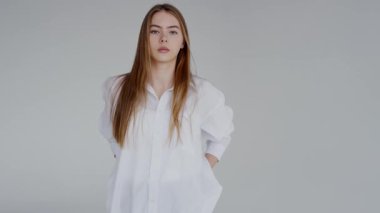 Portrait of a confident young woman in a casual pose wearing a classic white shirt. Featuring a minimalist style and a neutral background.Confident Young Woman in a Stylish White Shirt Posing Casually