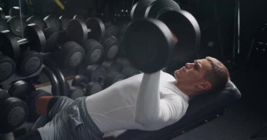 Focused young male with determination lifting weights in a well-equipped gym. Capture of fitness routine and muscular development. Young Man Doing Bench Press Exercise in Modern Gym