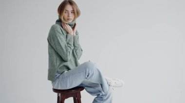 Portrait of a beautiful young woman dressed in a thick, cozy green sweater. She poses with a contemplative expression against a plain background, exuding a sense of warmth and introspection.