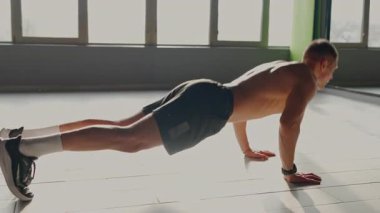 Focused and fit young man doing push-ups in a sunlit gym, displaying strength and dedication in a modern fitness setting. Fit Young Man Performing a Perfect Push-Up in a Bright Gym