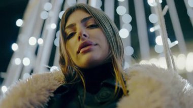 Geceleri şehir merkezinde poz veren güzel bir kadın. Sokaktaki doğal güzellik kraliçesi. Ağır çekim. Akşam şehirde yürürken kameraya bakan kendine güvenen güzel bir kadının portresi.