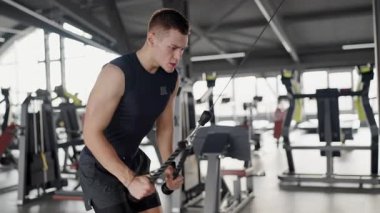 Focused young male athlete using a cable machine at a modern gym. This image captures the dedication and effort in fitness training. Young Man Working Out at Gym Using Cable Machine Strength Training