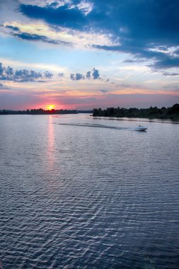 gün batımında nehrin üzerinde bir motorlu tekne yelken