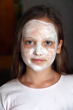 Yüzünde beyaz kozmetik maske olan bir kız.