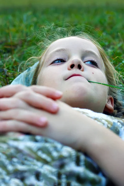 小さな女の子は彼女の口で草のブレードと腕を組んで草に横たわる — ストック写真