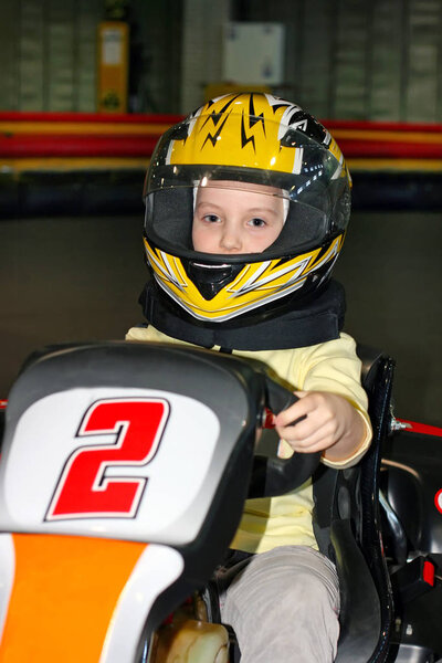 Улыбающаяся маленькая девочка в шлеме в картинге на картинговой дорожке в помещении

