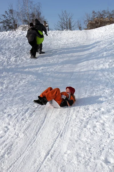 雪の丘の下のオレンジ色のオーバー オール スライドの小さな女の子 — ストック写真