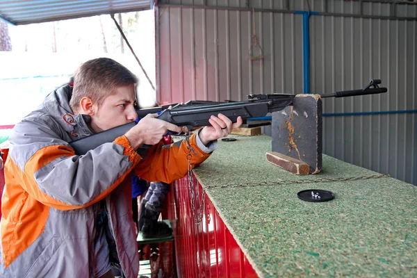 A teenager aims out of a rifle at a shooting range outdoors