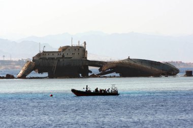 Batık bir geminin paslı kalıntıları arka plan üzerinde bir tekne dalgıçlar Denizi ile. Uzaktan dağlar görülebilir