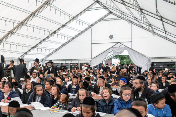 Uman,Ukraine, 13.09.2015: A lot of Jewish children in Kippahs and black clothes are indoors are sitting at the table with copy-books. Adults Jews stand in aisle. They gathered on celebration Rosh Hashanah, Jewish New Year